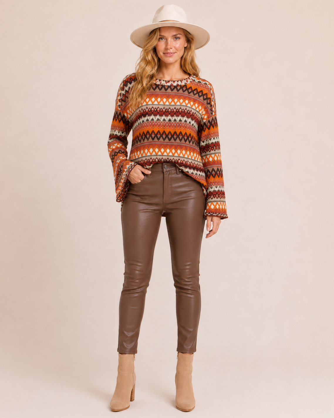 Full-body view of a woman wearing an orange striped knit pullover sweater with brown pants and a brown hat on a beige background