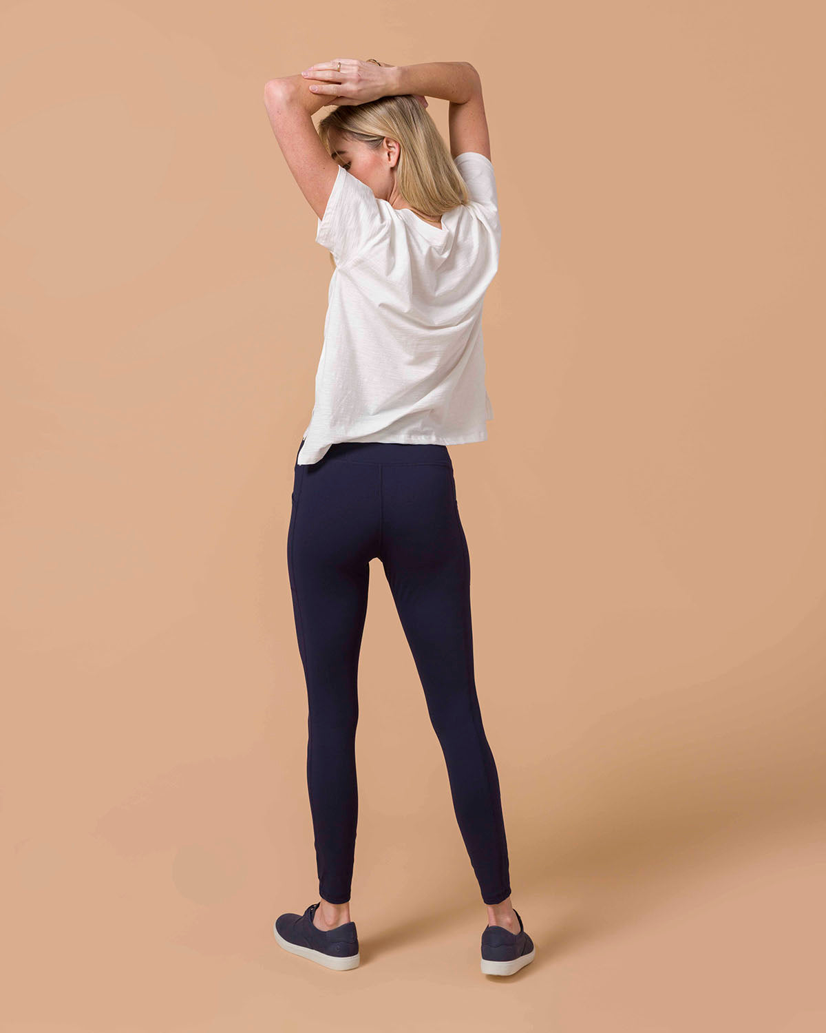 Blond woman wearing Navy Squat Proof Leggings with White top back view.