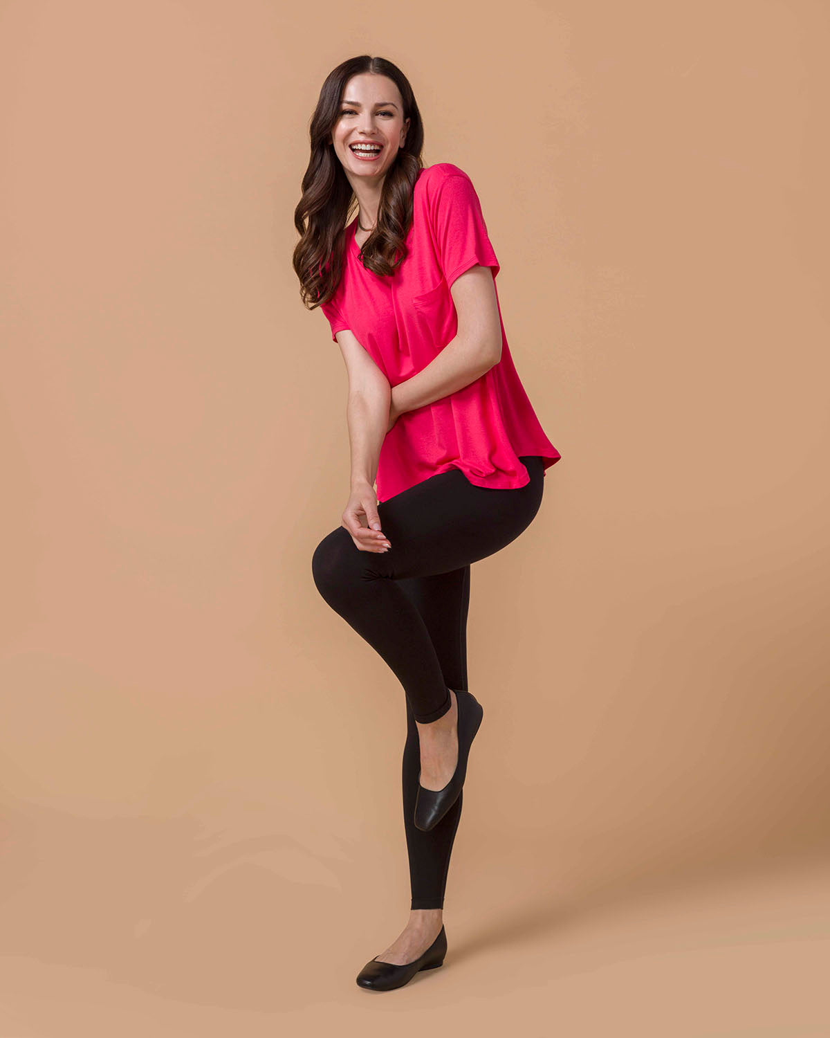 Woman wearing a Perfect Fit Pocket Tee - Canyon Red and black leggings on a beige background