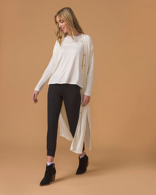 Ivory Ribbed Long Duster Cardigan Long cream cardigan worn by a woman with white top and black pants, beige background