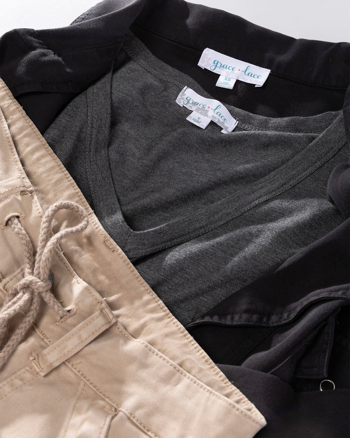 Flat lay of a dark gray v-neck shirt layered under a black jacket next to beige pants
