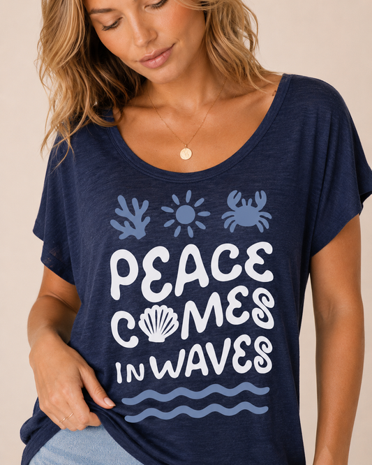 Peace Comes in Waves Graphic Tee Front view of a woman wearing a navy graphic tee featuring a "Peace Comes in Waves" design and light wash denim shorts on a beige background