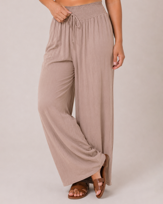 Smocked Waist Wide Leg Pant Mocha A woman modeling a dusty rose two-piece lounge set consisting of a lightweight open-front cardigan with lace trim and matching wide-leg drawstring pants, styled over a white tank top and brown slide sandals against a solid light beige studio background.