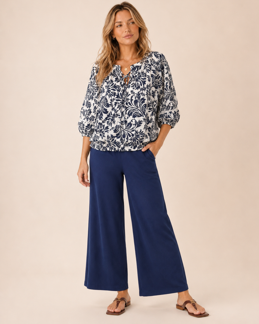Whispering Bloom Peasant Top Front view of a woman wearing a white and navy floral peasant top and navy wide-leg pants on a beige background