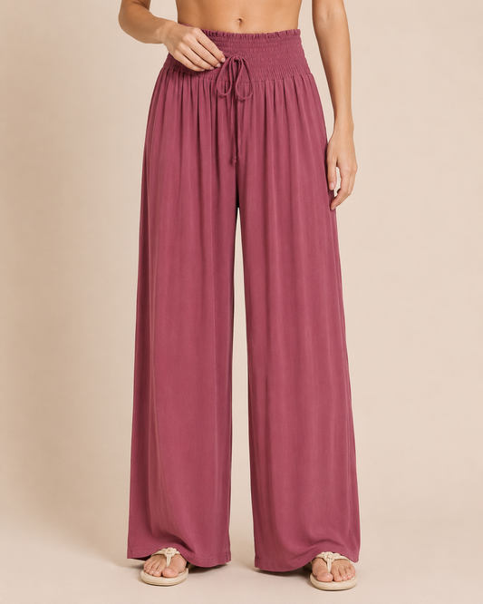 Smocked Waist Wide Leg Pant Rosewood Full-body view of a woman wearing rosewood smocked waist wide-leg pants and a pink floral blouse on a beige background