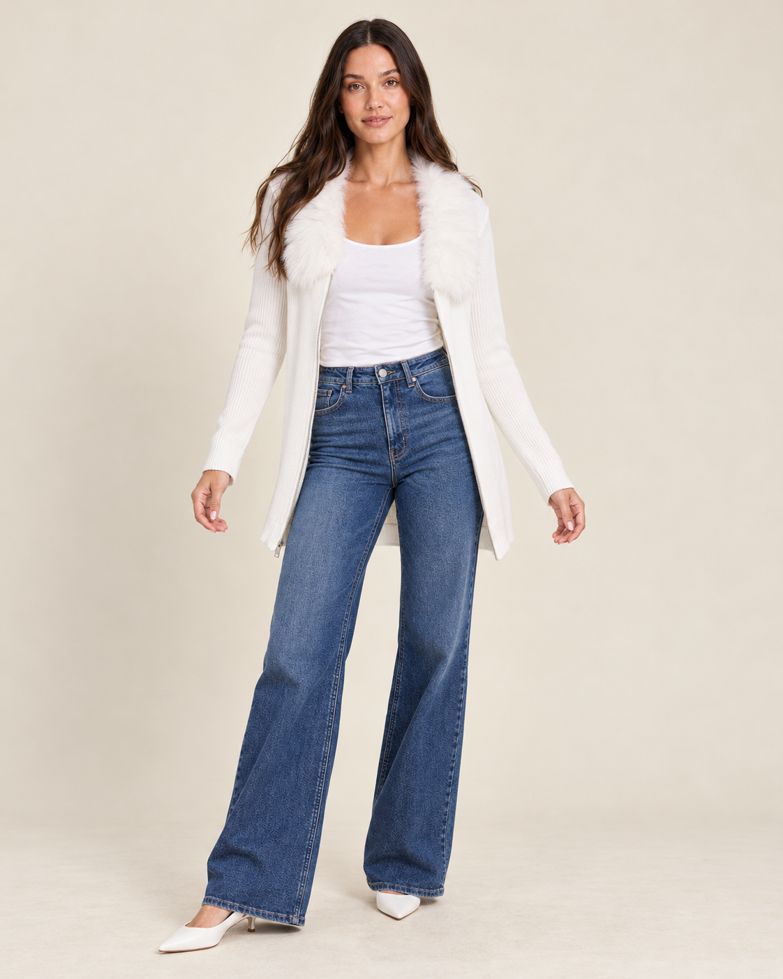 Full-body front view of a woman wearing a white hooded open-front cardigan over a white fitted top, paired with blue flared jeans and white sneakers on a beige background.