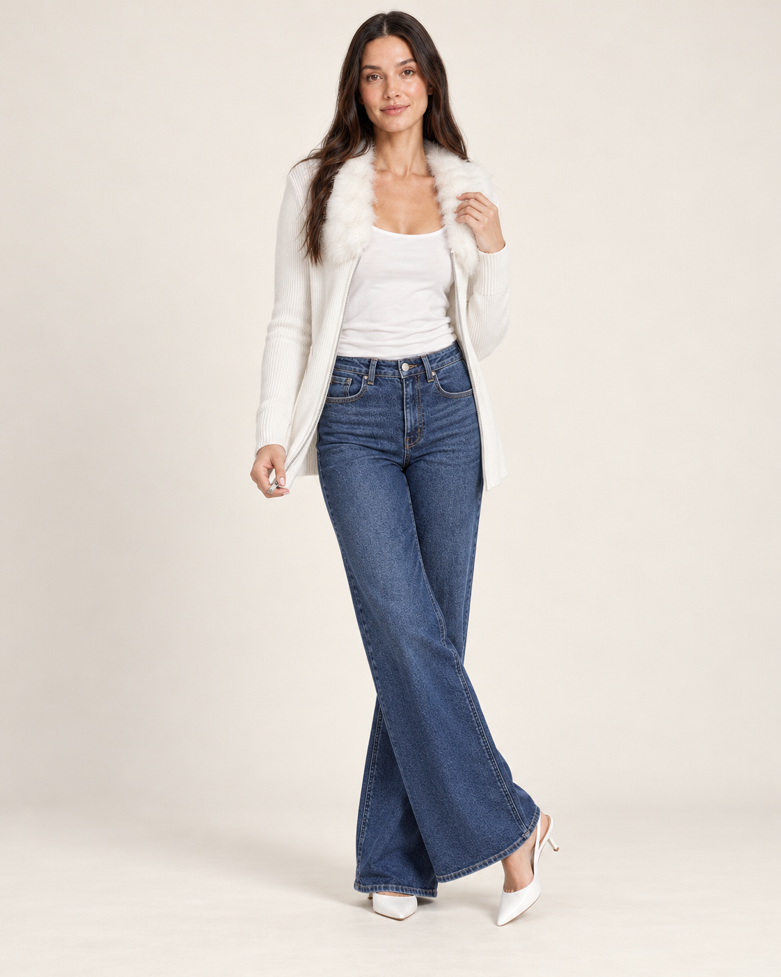 Full-body front view of a woman wearing a white hooded open-front cardigan over a white fitted top, paired with blue flared jeans and white sneakers on a beige background.