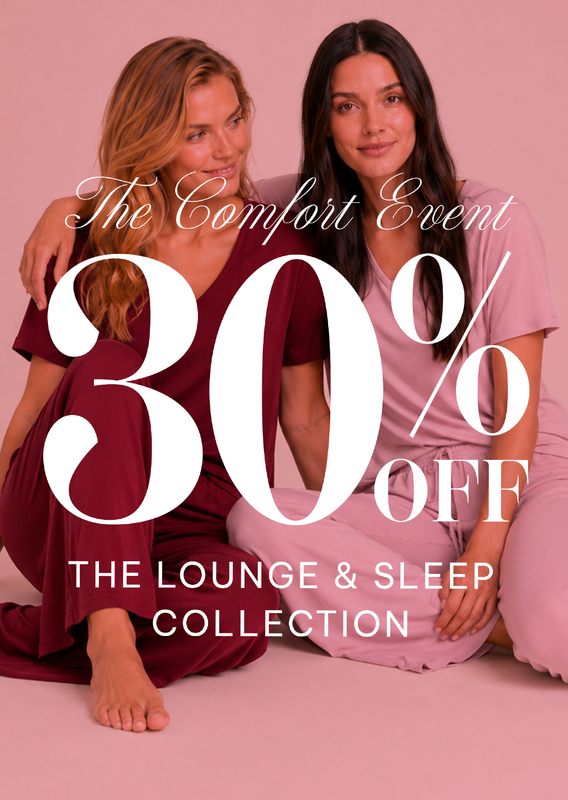 Two women sitting together in matching lounge sets against a pink studio background, with large overlaid text reading 'The Comfort Event 30% OFF THE LOUNGE & SLEEP COLLECTION.' Because people are present, this is classified as Lifestyle rather than Product/Packaging, even though the background is studio-clean.