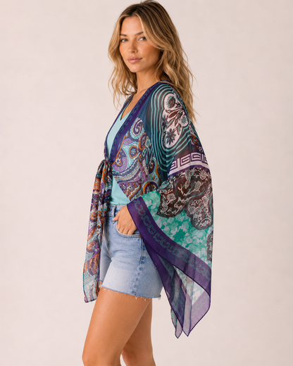 Side view of a woman wearing a blue floral front-tie kimono over a blue V-neck tank top and light wash denim shorts on a beige background