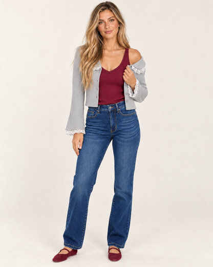 Full-body front view of a woman wearing a burgundy sleeveless V-neck tank top with blue jeans and red shoes on a beige background.