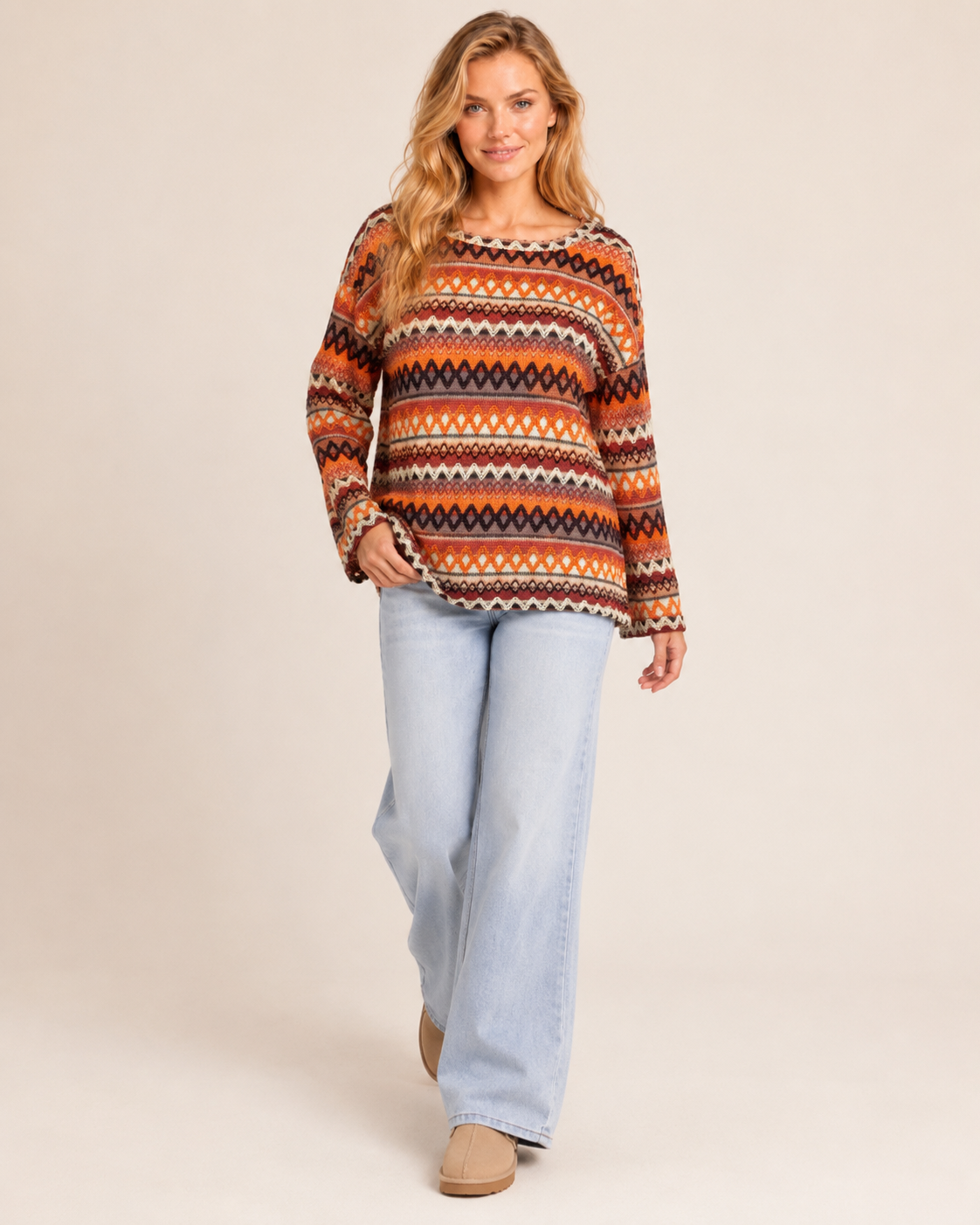 Full-body view of a woman wearing an orange striped knit pullover sweater with denim pants a beige background