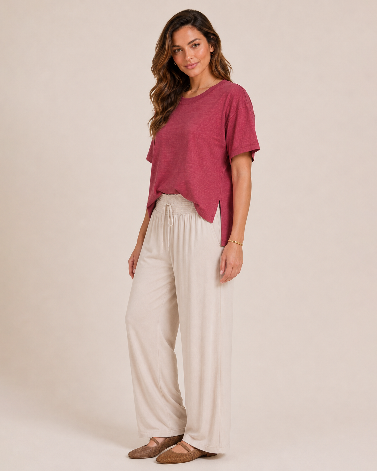 Side view of a woman wearing a Berry Ice cotton slub tee with white wide-leg pants on a beige background