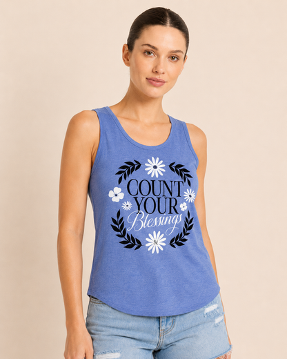 Close-up of a woman wearing a blue graphic tank top featuring a "Count Your Blessings" floral design and light wash denim shorts on a beige background