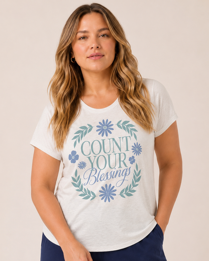 Close-up of a woman wearing a white graphic tee featuring a "Count Your Blessings" floral design and navy wide-leg pants on a beige background