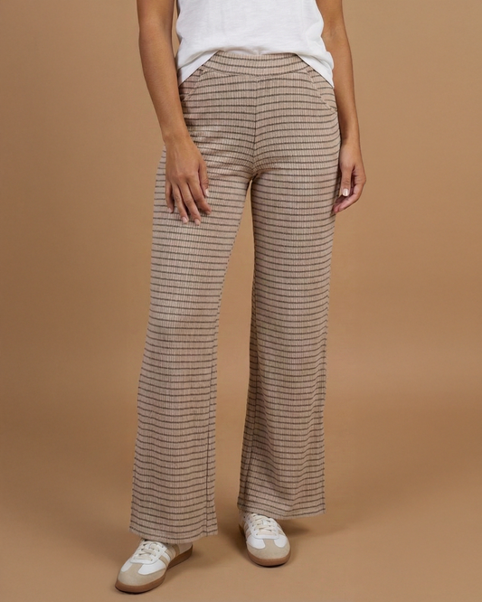 Woman wearing a white t-shirt and beige striped pants on a brown background
