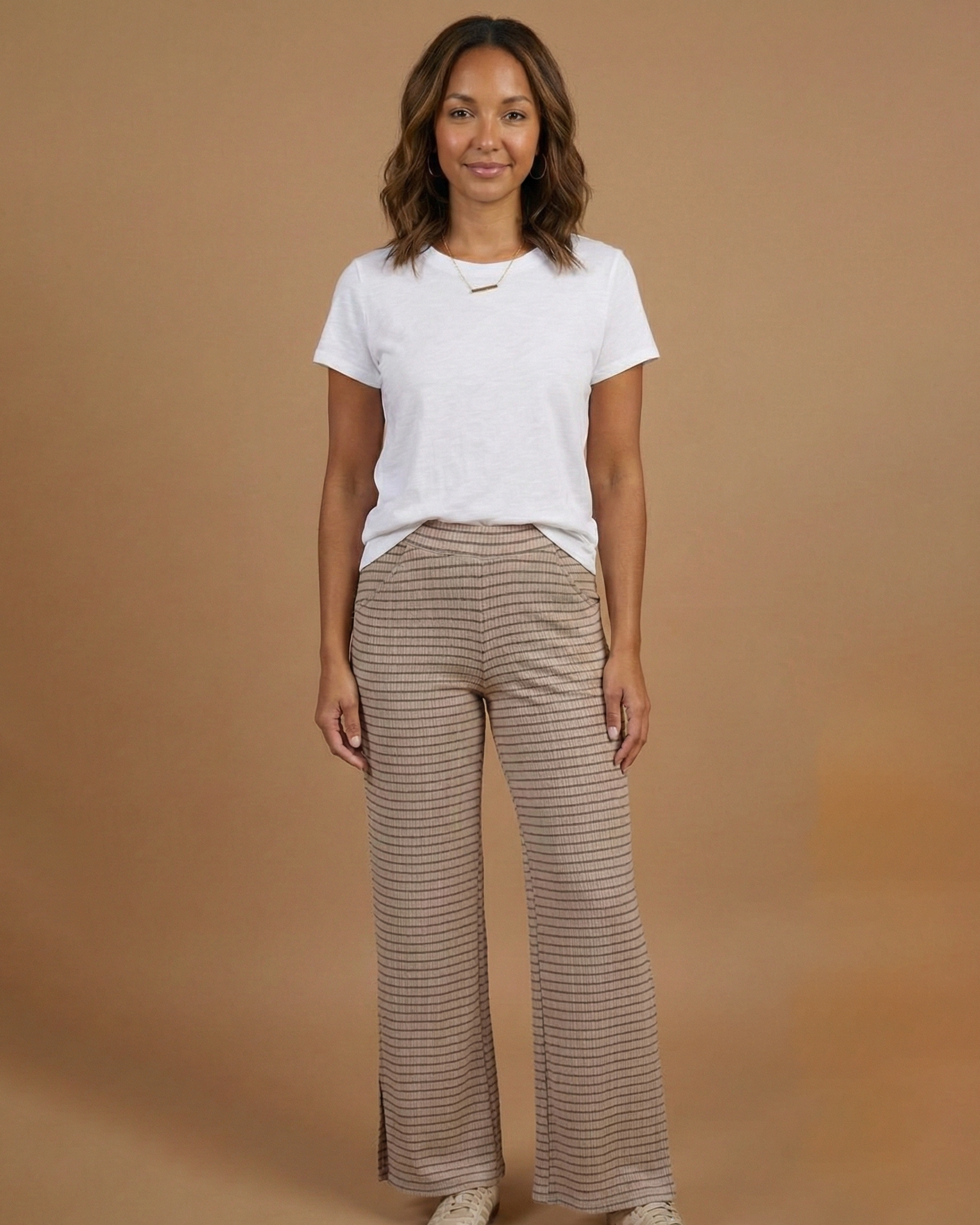 Woman wearing a white t-shirt and beige striped pants on a brown background