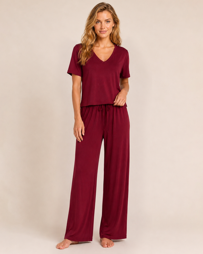 Full-body view of a woman wearing cabernet wide-leg pajama pants with a matching top on a beige background