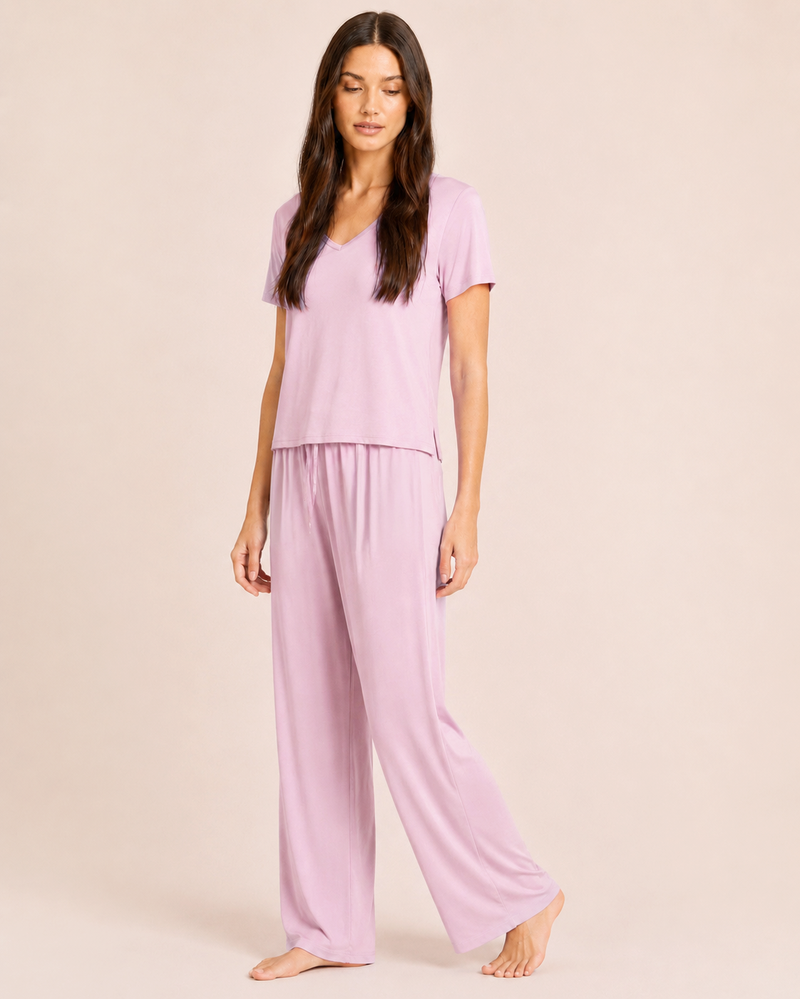 Full-body view of a woman wearing a Mauve Mist V-neck pajama top with matching wide-leg pants on a beige background
