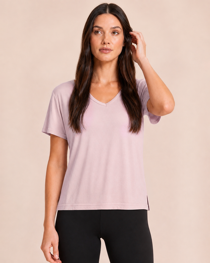 Close up view of a woman wearing a Mauve Mist V-neck pajama top with black pants on a beige background