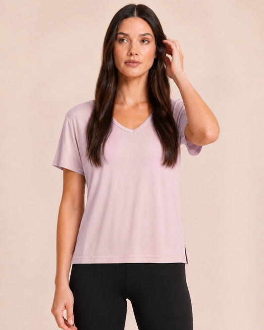 Close up view of a woman wearing a Mauve Mist V-neck pajama top with black pants on a beige background