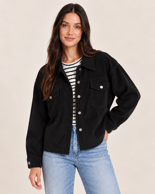 Cropped front view of a woman wearing an open black button-front cardigan over a black and white striped top, paired with light wash jeans on a beige background.