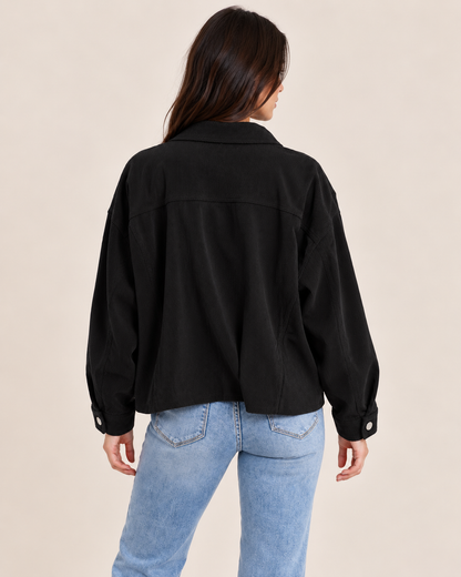 Back view of a woman wearing a black cardigan with light wash straight-leg jeans, showcasing the relaxed fit and back of the cardigan on a beige background.