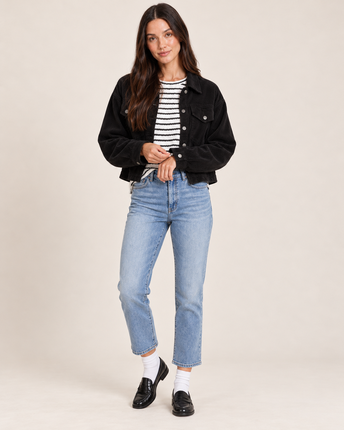 Full-body front view of a woman wearing a black button-front cardigan over a black and white striped top, paired with light wash straight-leg jeans and black shoes on a beige background.