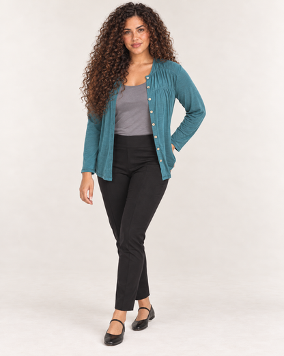Full-body front view of a woman wearing black ankle-length leggings with a teal cardigan and black Mary Jane shoes on a beige background