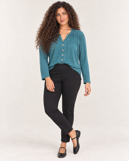 Full-body front view of a woman wearing black ankle-length leggings with a teal cardigan and black Mary Jane shoes on a beige background