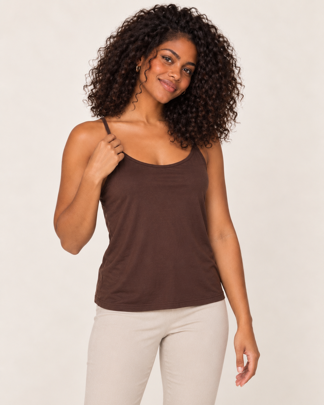 Cropped front view of a woman wearing a brown spaghetti-strap tank top with white pants on a beige background