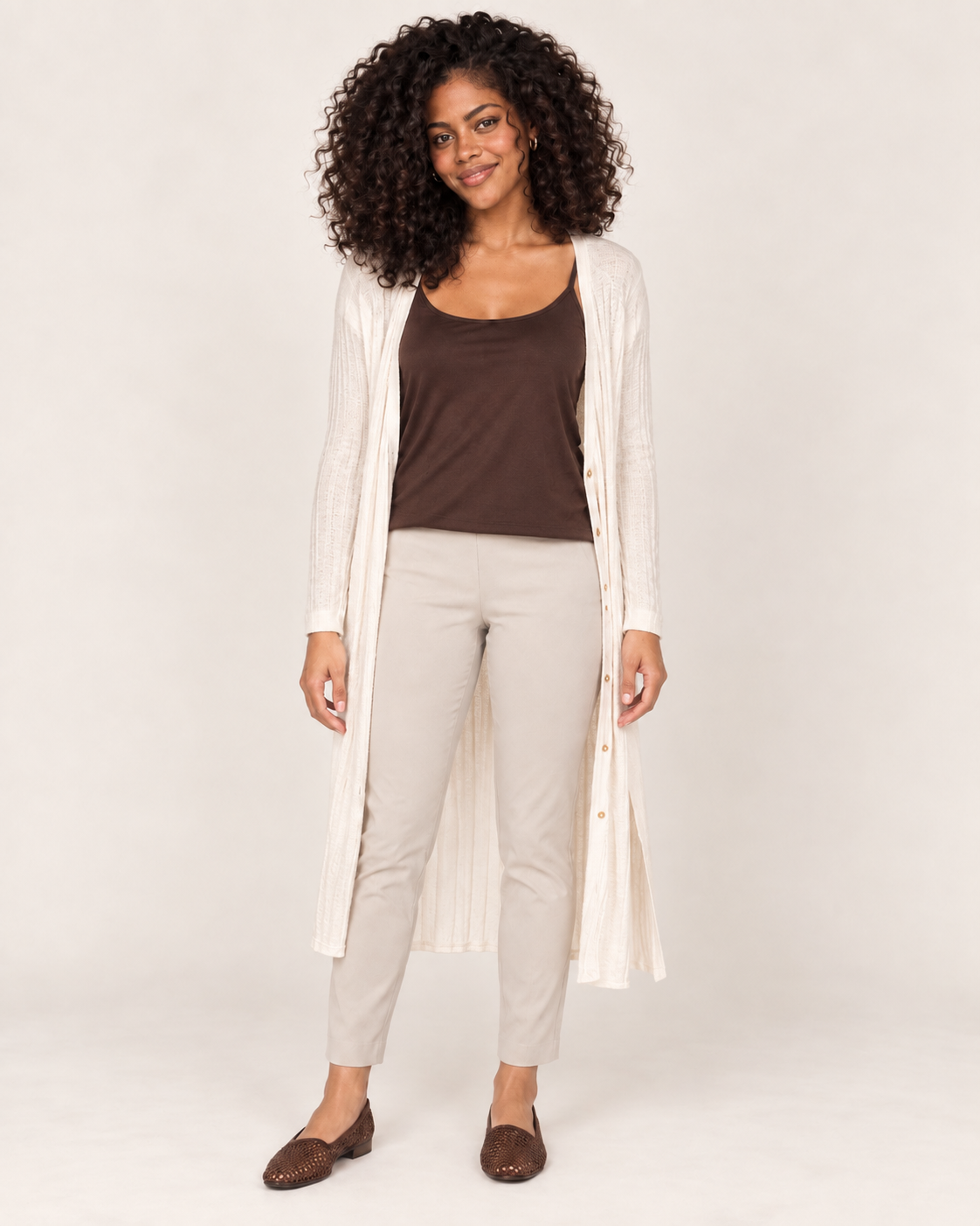 Full-body front view of a woman wearing a brown spaghetti-strap tank top with white wide-leg pants and white sneakers on a beige background