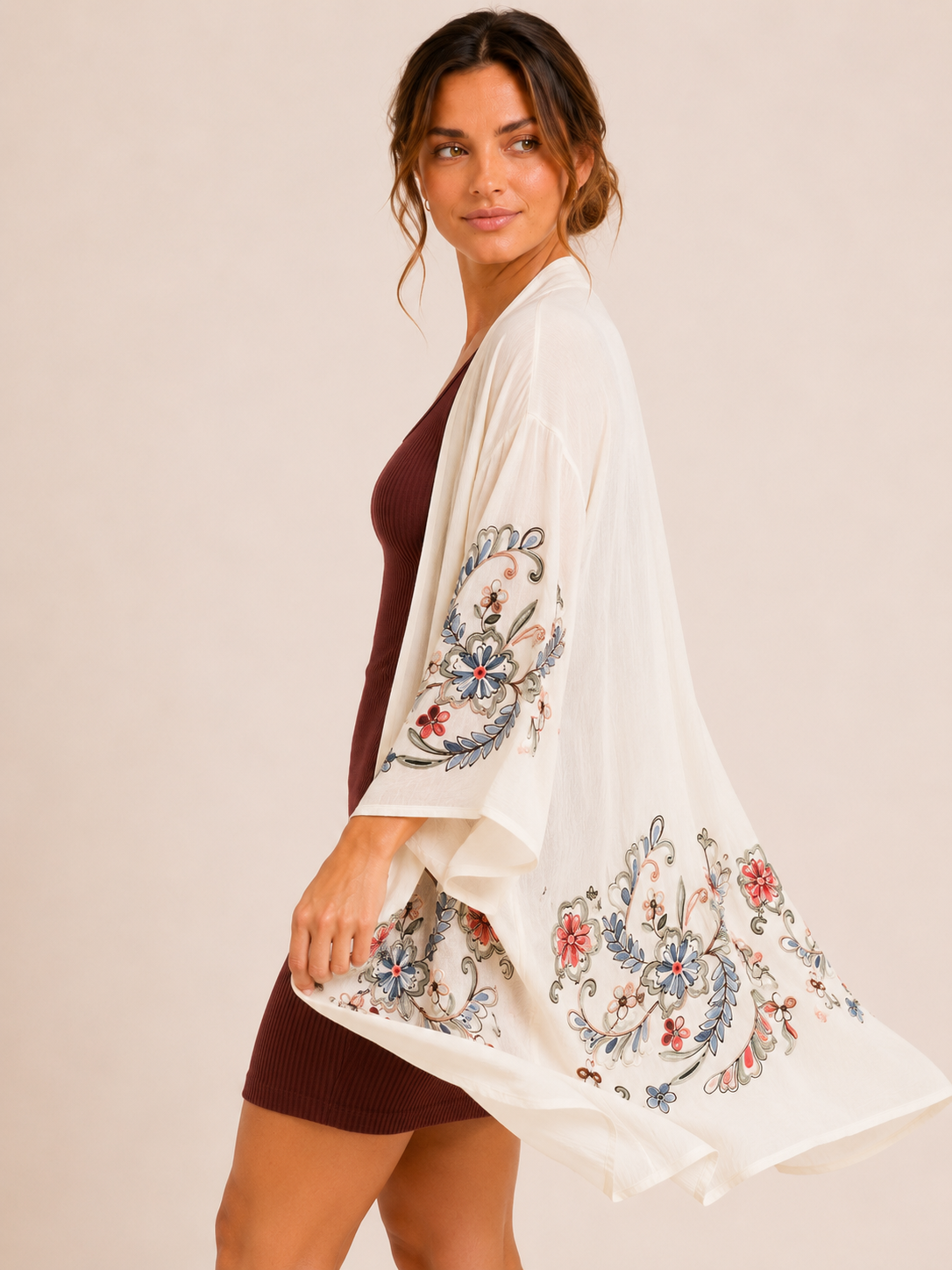 Side view of a woman wearing a cream floral kimono over a burgundy ribbed tank dress on a beige background