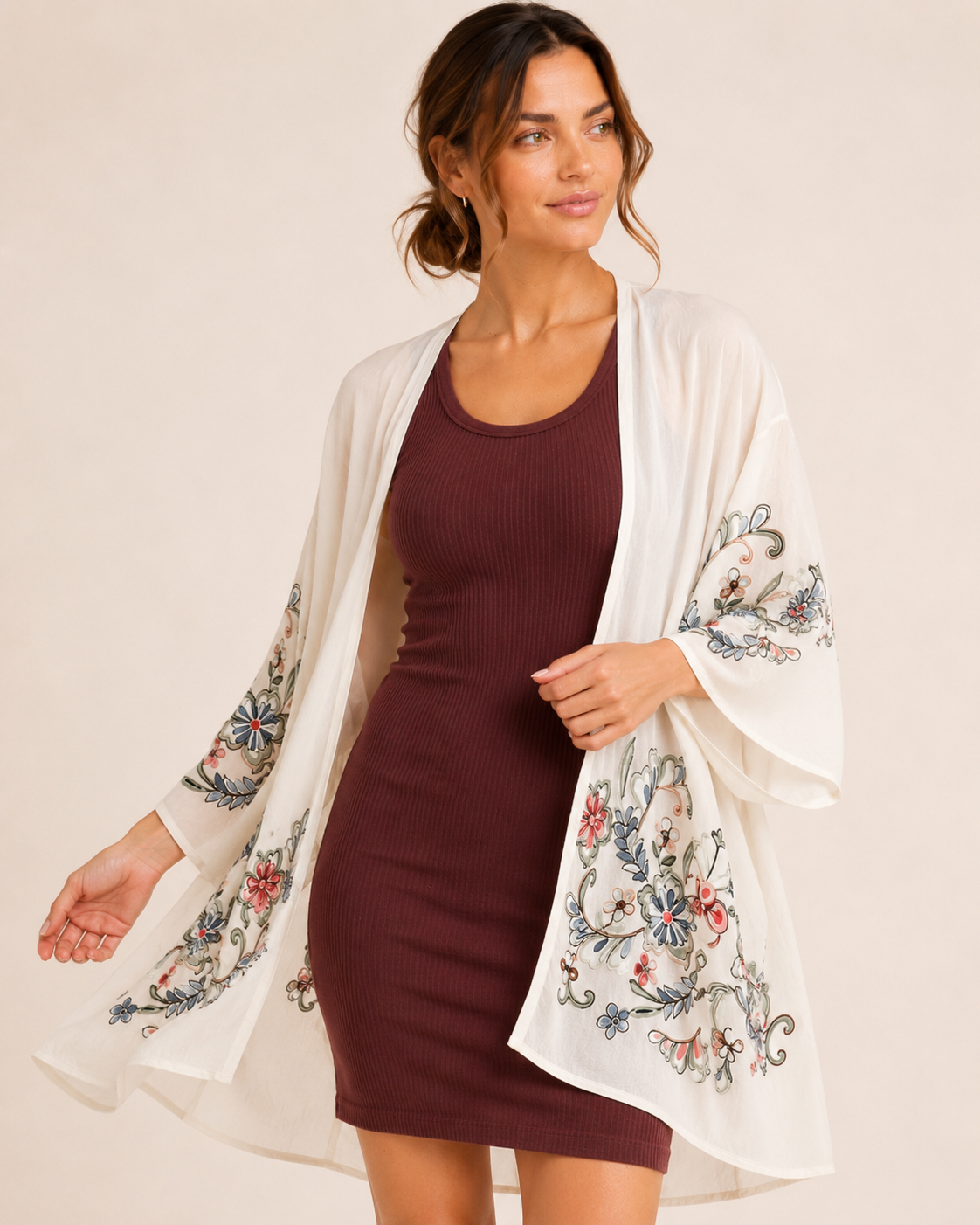 Front view of a woman wearing a cream floral kimono over a burgundy ribbed tank dress on a beige background