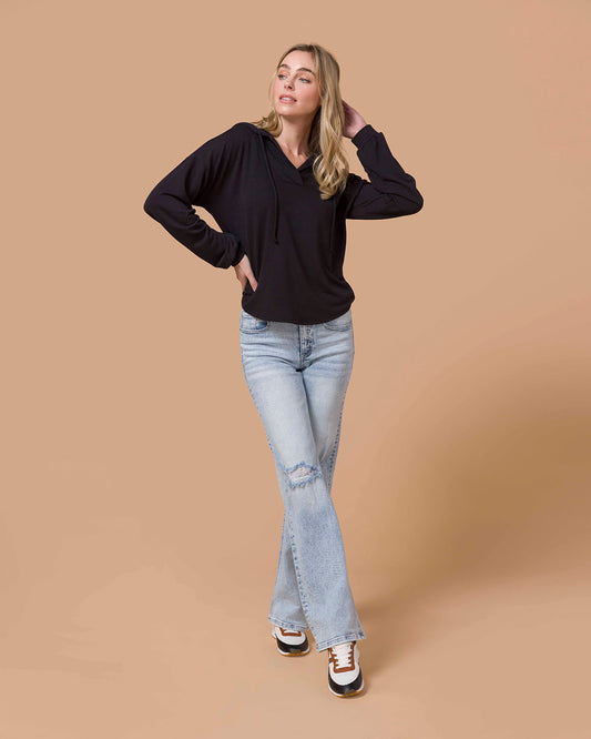 Black Pullover V-Neck Drawstring Hoodie on blond model sitting on stool.