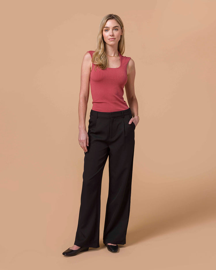 Woman wearing a pink sleeveless top and black pants on a beige background