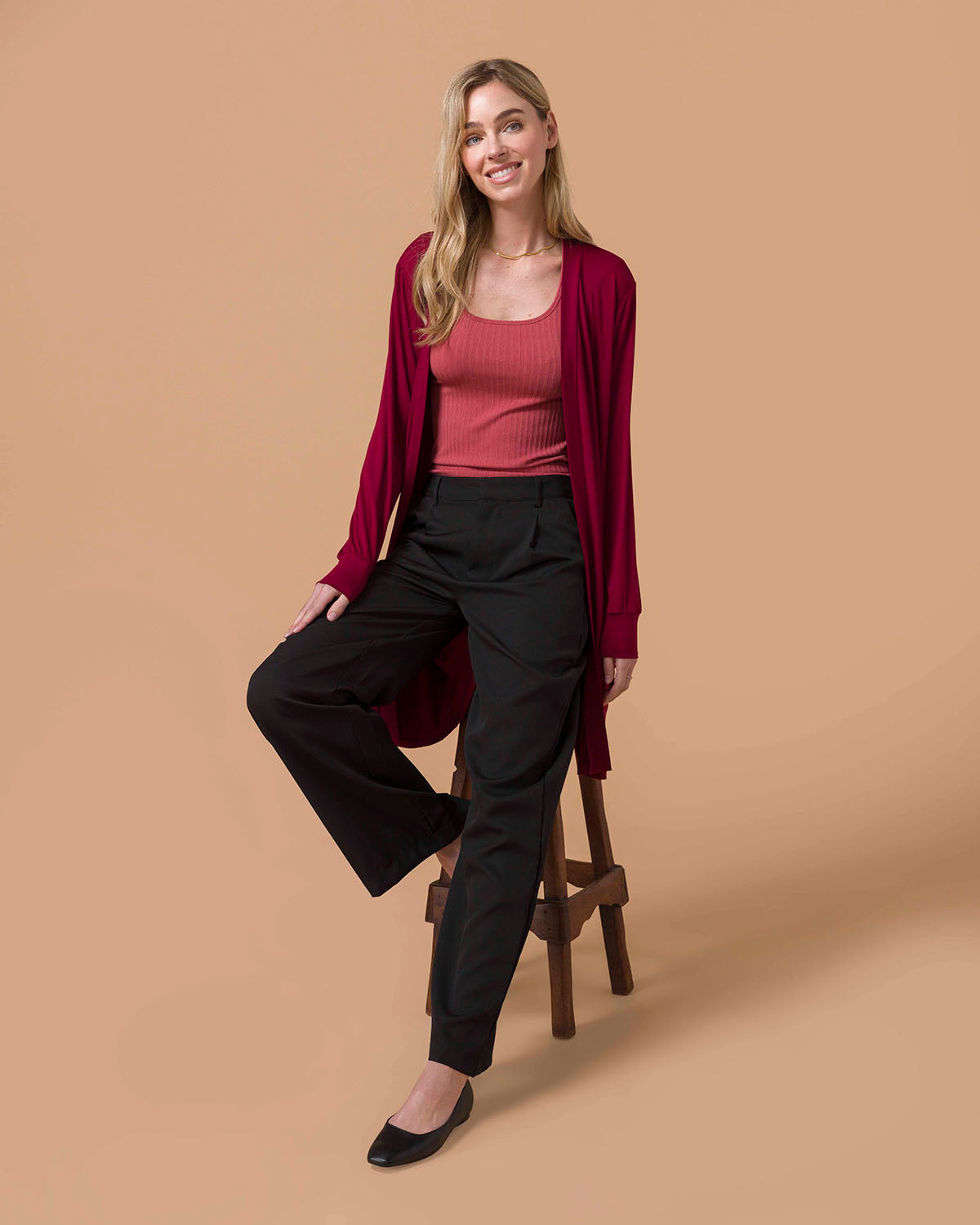 Woman wearing a pink top and black pants with a red cardigan on a beige background