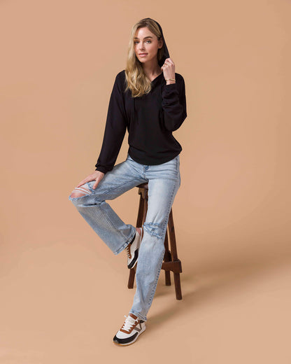 Black Pullover V-Neck Drawstring Hoodie on blond model sitting on stool.