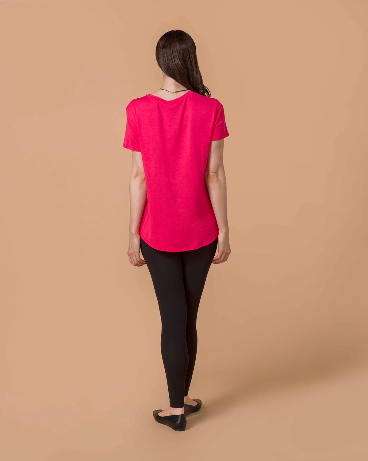 Woman wearing a Perfect Fit Pocket Tee - Canyon Red and black leggings on a beige background back view.
