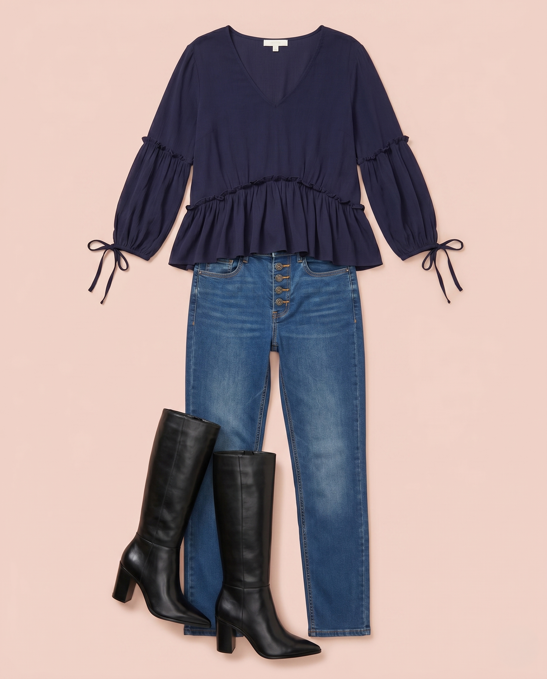 Navy blue peplum blouse with tie-sleeve details styled with blue jeans and black knee-high boots on a beige background