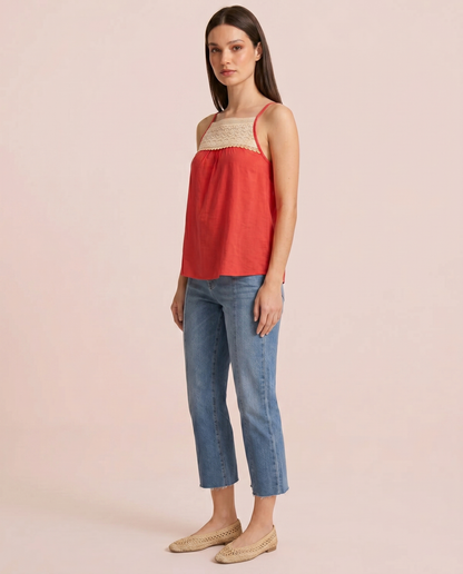 Side view of a woman wearing a coral camisole top with a crochet lace yoke and blue jeans on a beige background
