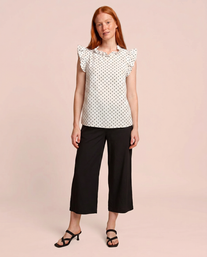 Front view of a woman wearing a white blouse with black polka dots and black pants on a beige background