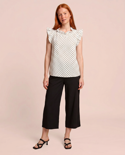 Front view of a woman wearing a white blouse with black polka dots and black pants on a beige background
