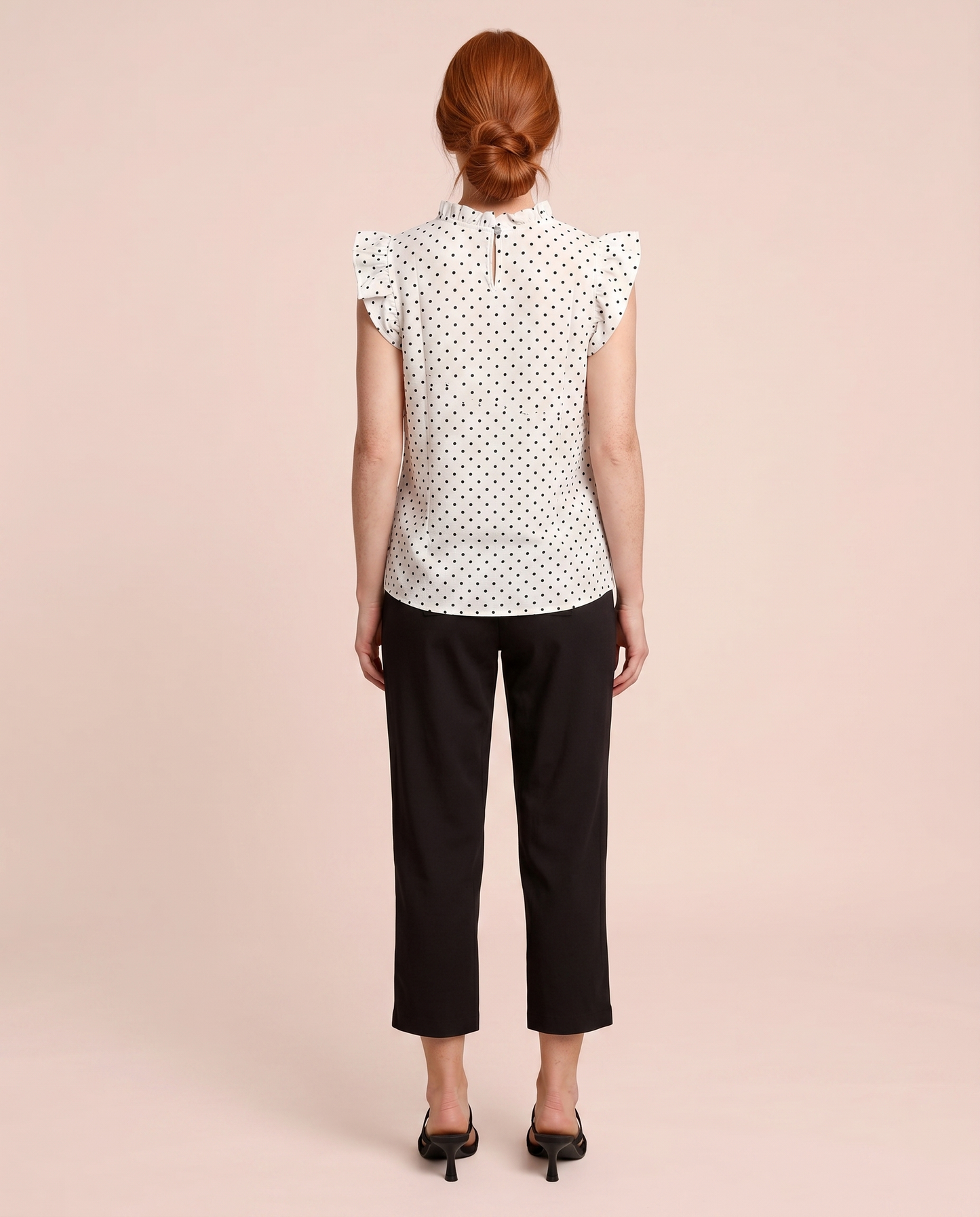 Back view of a woman wearing a white blouse with black polka dots and black pants on a beige background
