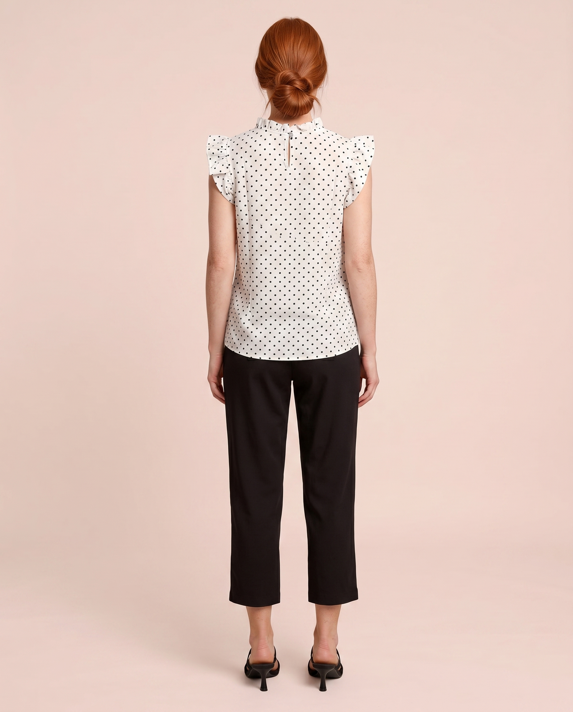 Back view of a woman wearing a white blouse with black polka dots and black pants on a beige background