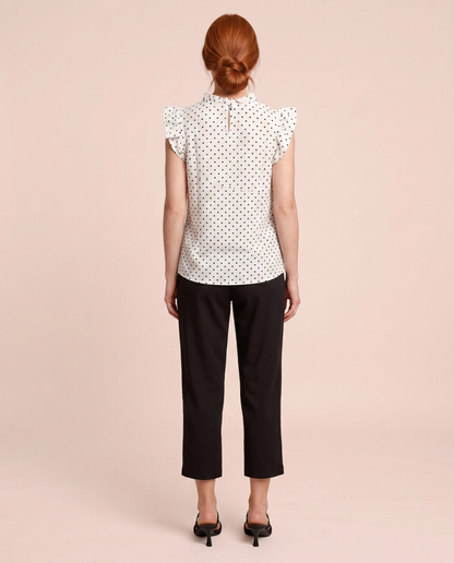 Back view of a woman wearing a white blouse with black polka dots and black pants on a beige background