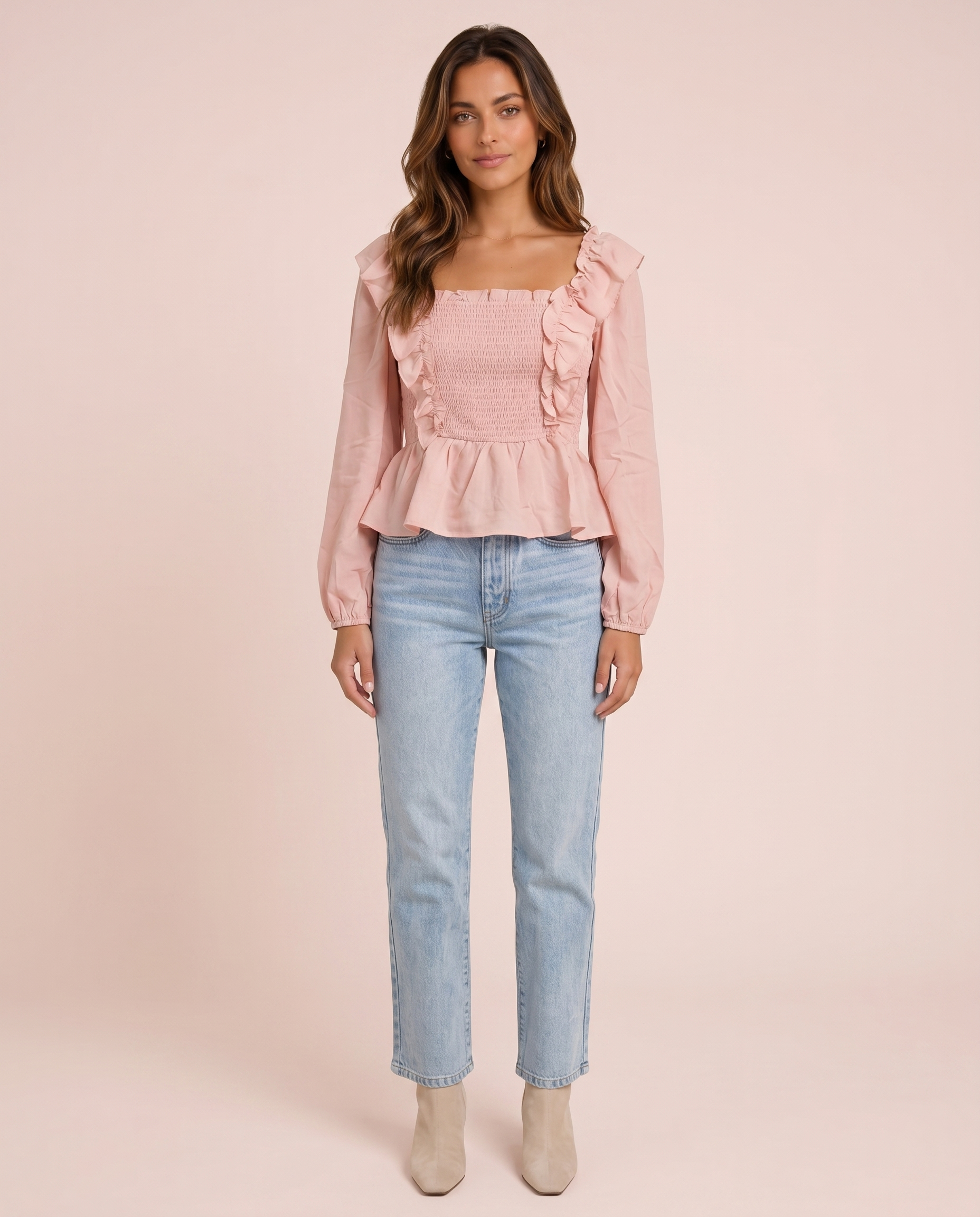Woman wearing a pink ruffled peplum blouse and light blue jeans on a pink background