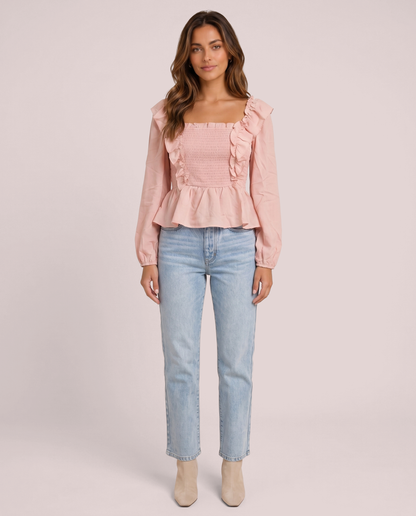 Woman wearing a pink ruffled peplum blouse and light blue jeans on a pink background