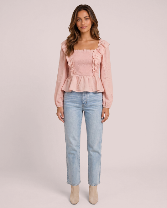 Woman wearing a pink ruffled peplum blouse and light blue jeans on a pink background