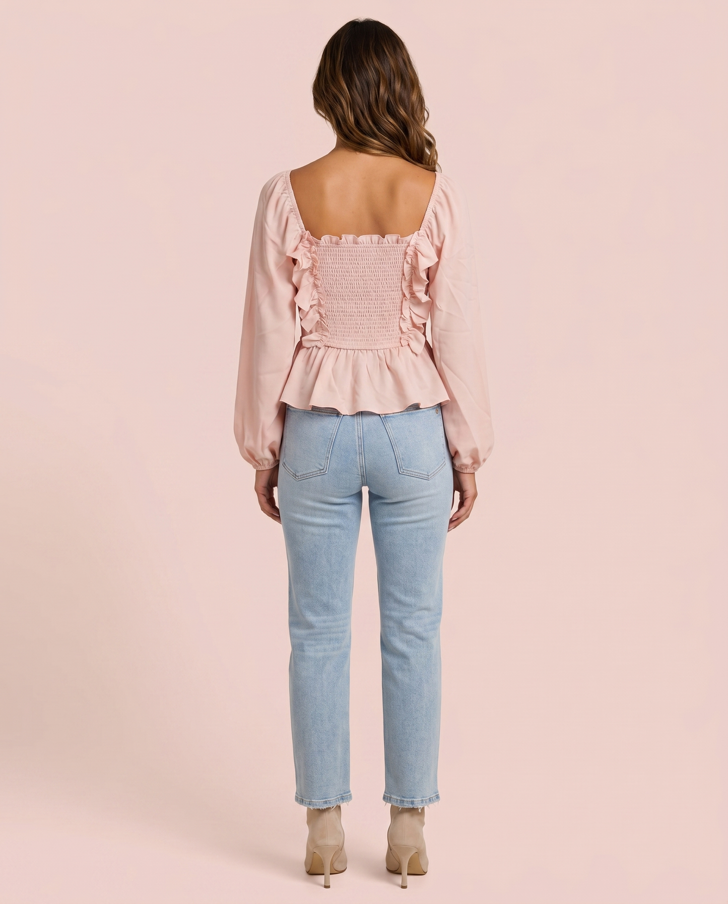 Back view of woman wearing a pink ruffled peplum blouse and light blue jeans on a pink background