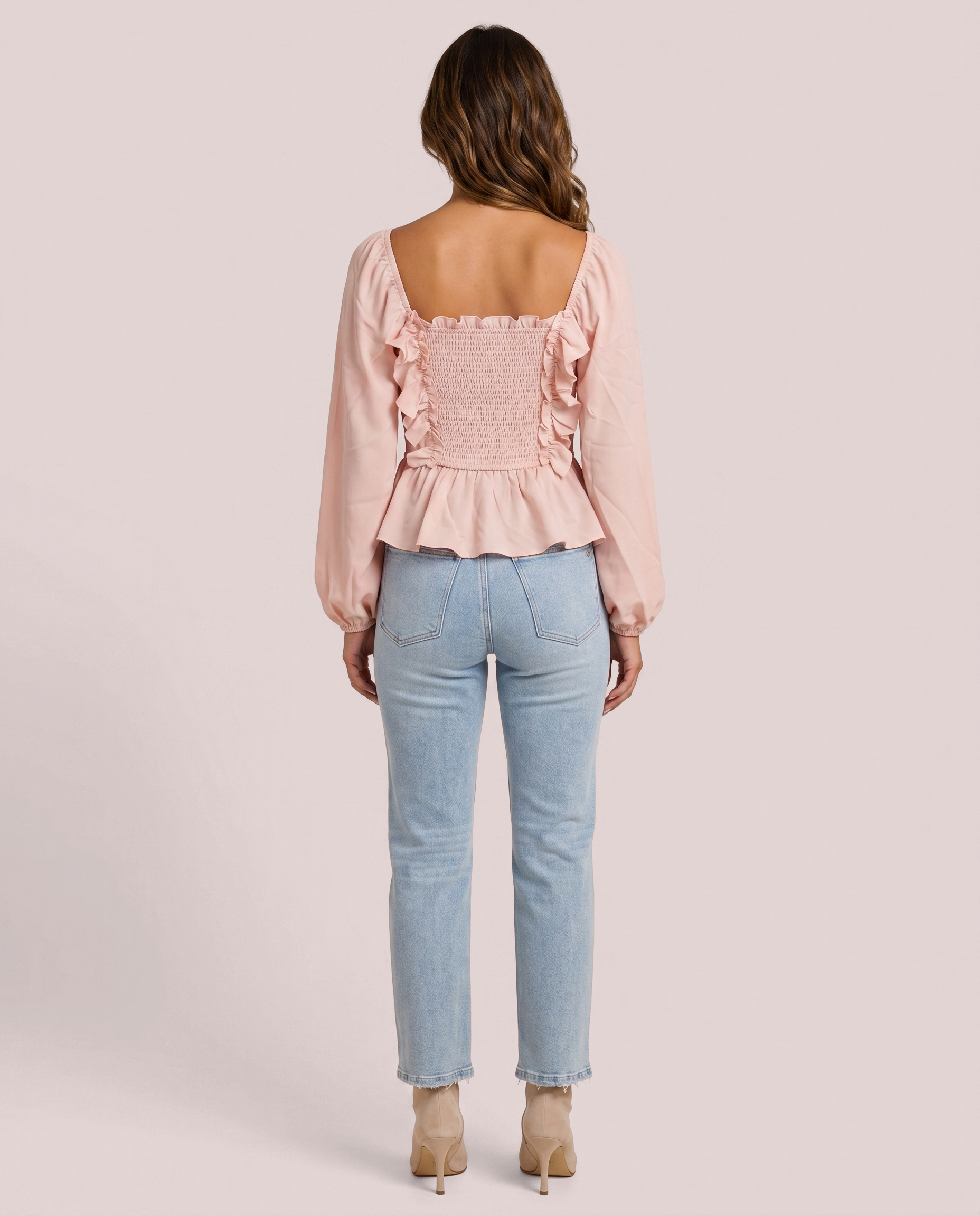 Back view of woman wearing a pink ruffled peplum blouse and light blue jeans on a pink background